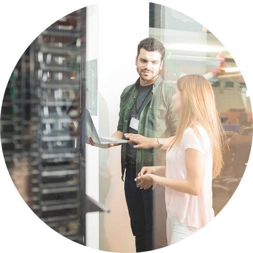 Colleagues speaking in server room, holding laptop